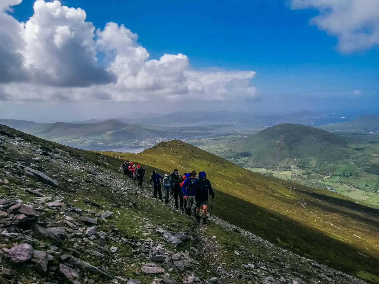 A line of club members walking up a ridge under a bright blue sky, with valleys and hills below