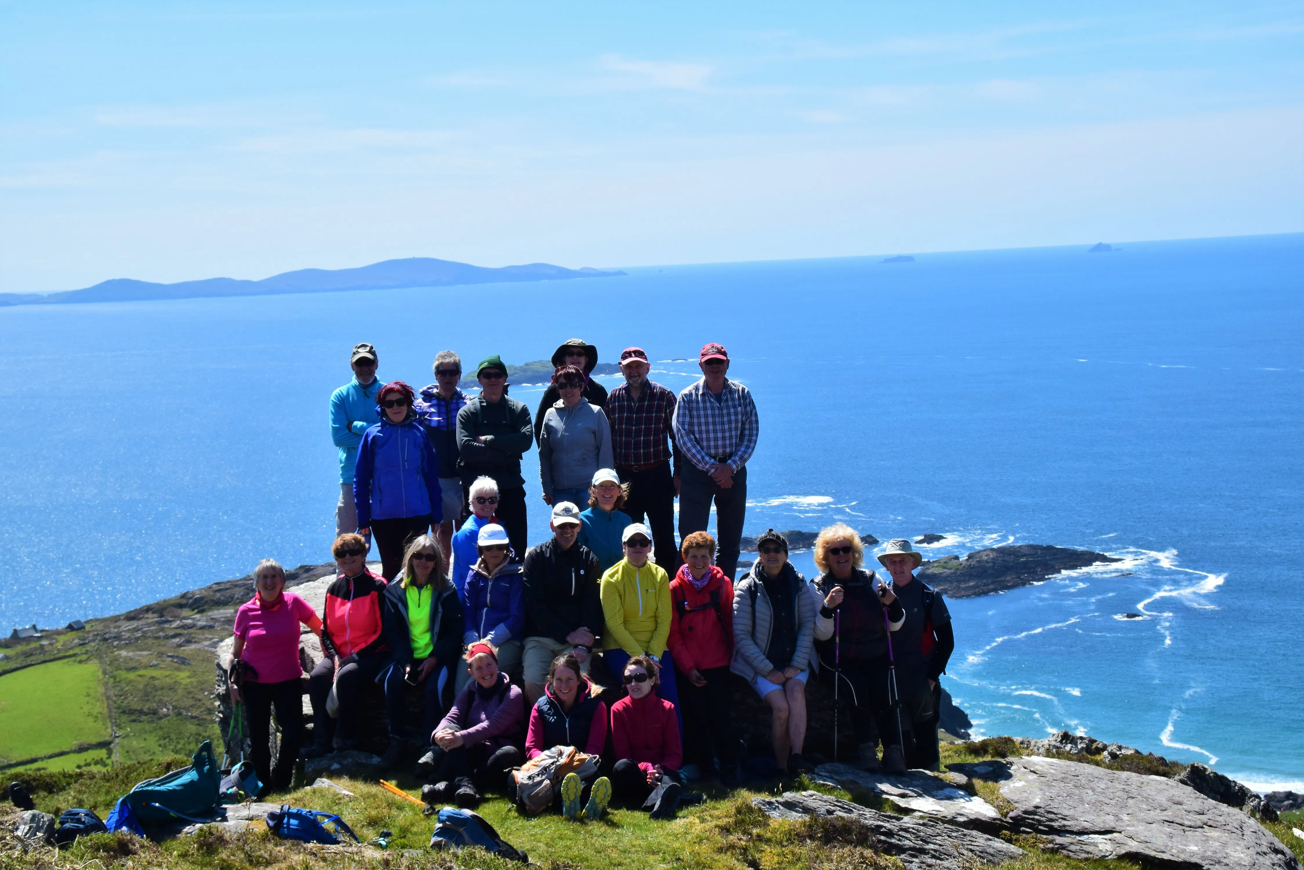 A large group of club members on a headland above the sea on a sunny day