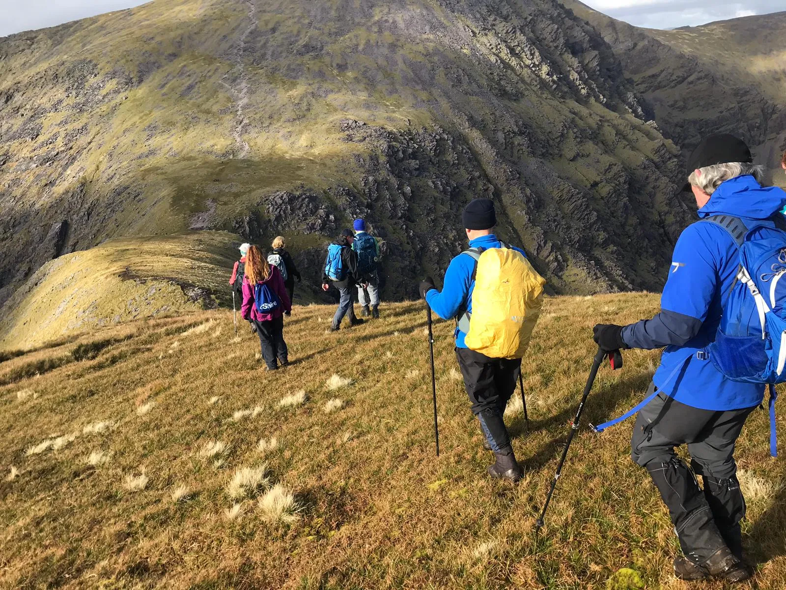 Club members walking along a grassy ridge with crags behind